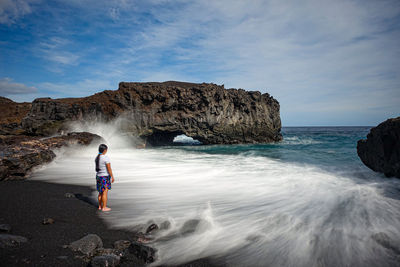 Full length of man on rock at beach against sky