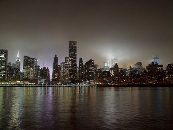 Illuminated buildings by river against sky in city at night