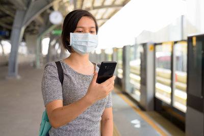 Young woman with mask using mobile phone while standing at station