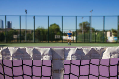 Close-up of net against man playing tennis court