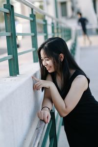 Smiling young woman standing by railing outdoors