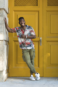 Cheerful young man standing against closed yellow doors