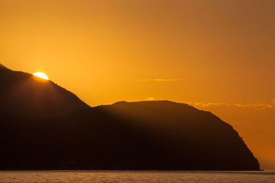 Scenic view of silhouette mountains by sea against orange sky