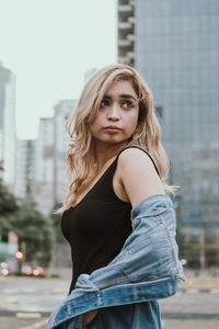 Beautiful young woman in denim jacket standing on street in city