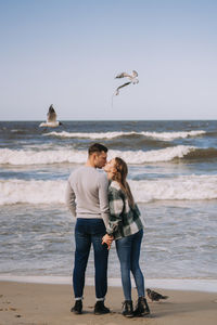 Full length of friends standing on beach against sky