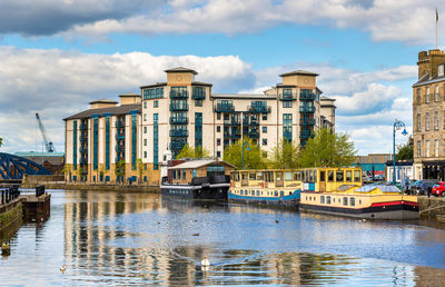 Boats moored in river by buildings against sky