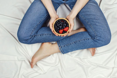 Low section of woman holding fruit on bed