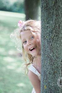 Portrait of playful girl hiding behind tree trunk