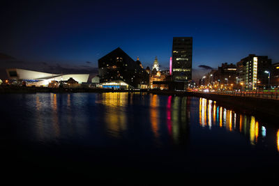 Illuminated buildings by river against clear sky at night