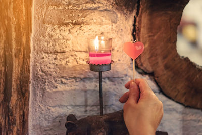 Cropped hand of person holding heart shape candle against wall