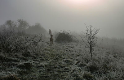 Woman walking on field against sky with dog