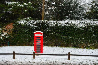 Red telephone booth against trees during winter