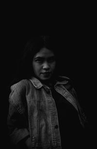 Portrait of young woman against black background