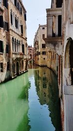 Canal amidst old buildings in city against sky