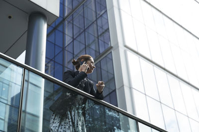 Businesswoman talking on mobile phone while leaning on railing against building