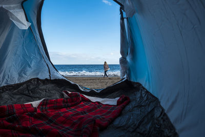 Woman walking on shore at beach seen through tent