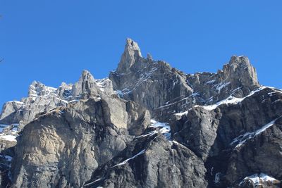 Low angle view of snowcapped mountains against clear blue sky