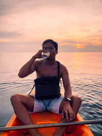 Man sitting on boat against sea during sunset