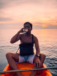 Man sitting on boat against sea during sunset