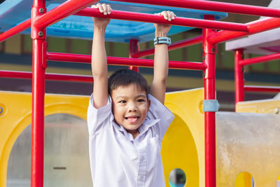 Smiling boy hanging at monkey bars at playground