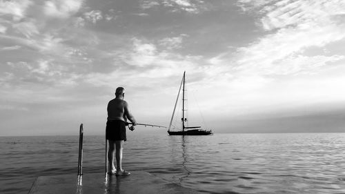 Rear view of man fishing at sea against sky