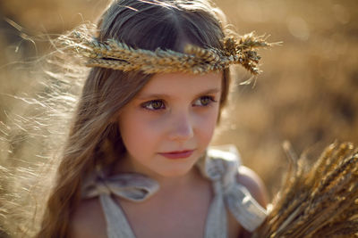 Girl child in a dress and a wreath on her head stands on a mown field of wheat at sunset in summer