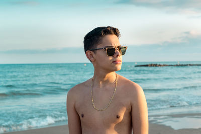 Young man wearing sunglasses standing at beach against sky