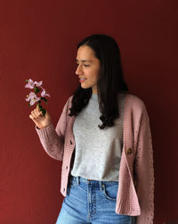 Full length of woman holding flower standing against colored background