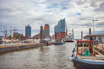 Boats moored in river by buildings against sky