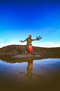 Woman with arms outstretched standing in water against clear blue sky