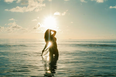 Woman standing in sea against sky during sunset