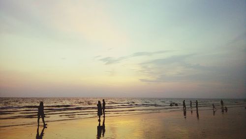 Silhouette people on beach against sky during sunset