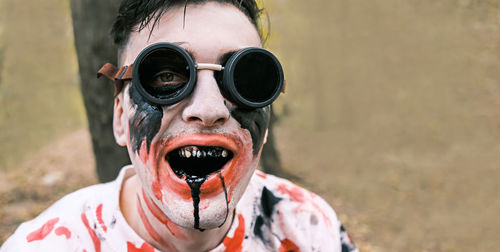 Portrait is close-up of face of zombie with traces of blood and black fluid flowing from the mouth. 