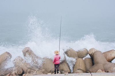 Full length of man fishing on rock in sea