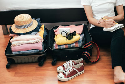 Midsection of woman writing in book by suitcase while sitting on floor at home