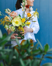 Woman in flowing yellow skirt and white shirt with bouquet in glass vase against the blue background