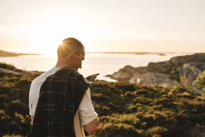 Rear view of man standing on land against sky during sunset