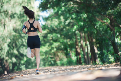 Full length rear view of young woman jogging on road amidst trees