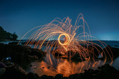 Man spinning wire wool while standing at sea against clear sky at night