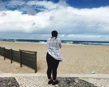 Rear view of woman standing at beach against cloudy sky