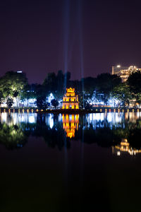 Illuminated city by lake against sky at night