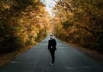 Portrait of man on road amidst trees during autumn