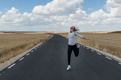 Woman jumping on road against sky