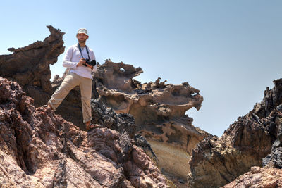 Man with camera standing on rock formation against sky