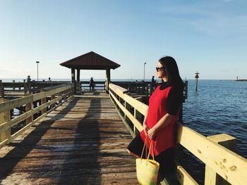 Woman standing on pier by sea against sky