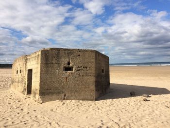 Built structure on sandy beach against cloudy sky