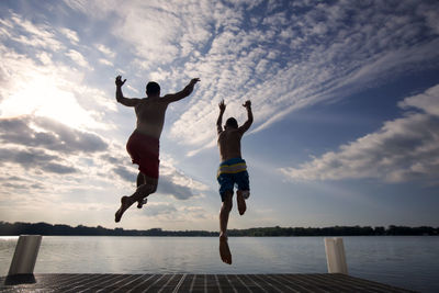 Rear view of father and son from pier at lake against sky