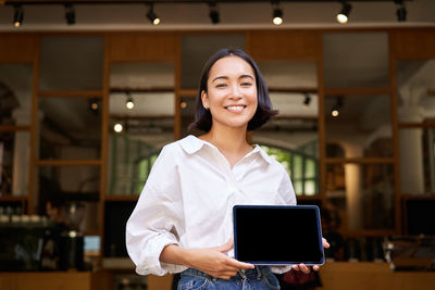 Portrait of young woman using laptop while standing in cafe