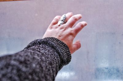 Cropped hand of woman gesturing against wet window during rainy season