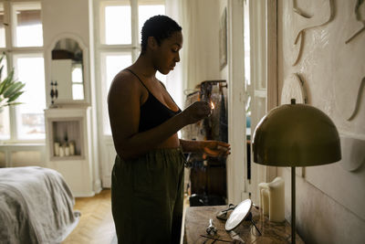 Side view of young woman holding lit matchstick at home